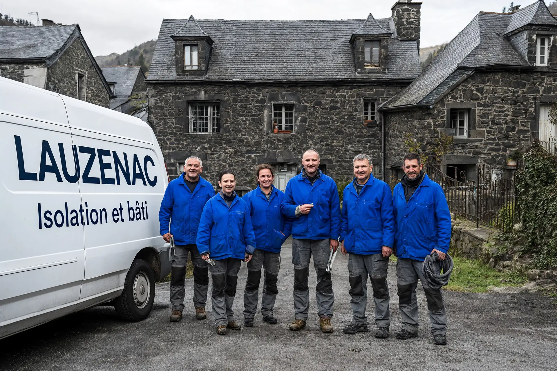 L’équipe de Lauzenac, six artisans en veste de travail bleue, devant le fourgon de l’entreprise et une maison de pierre.