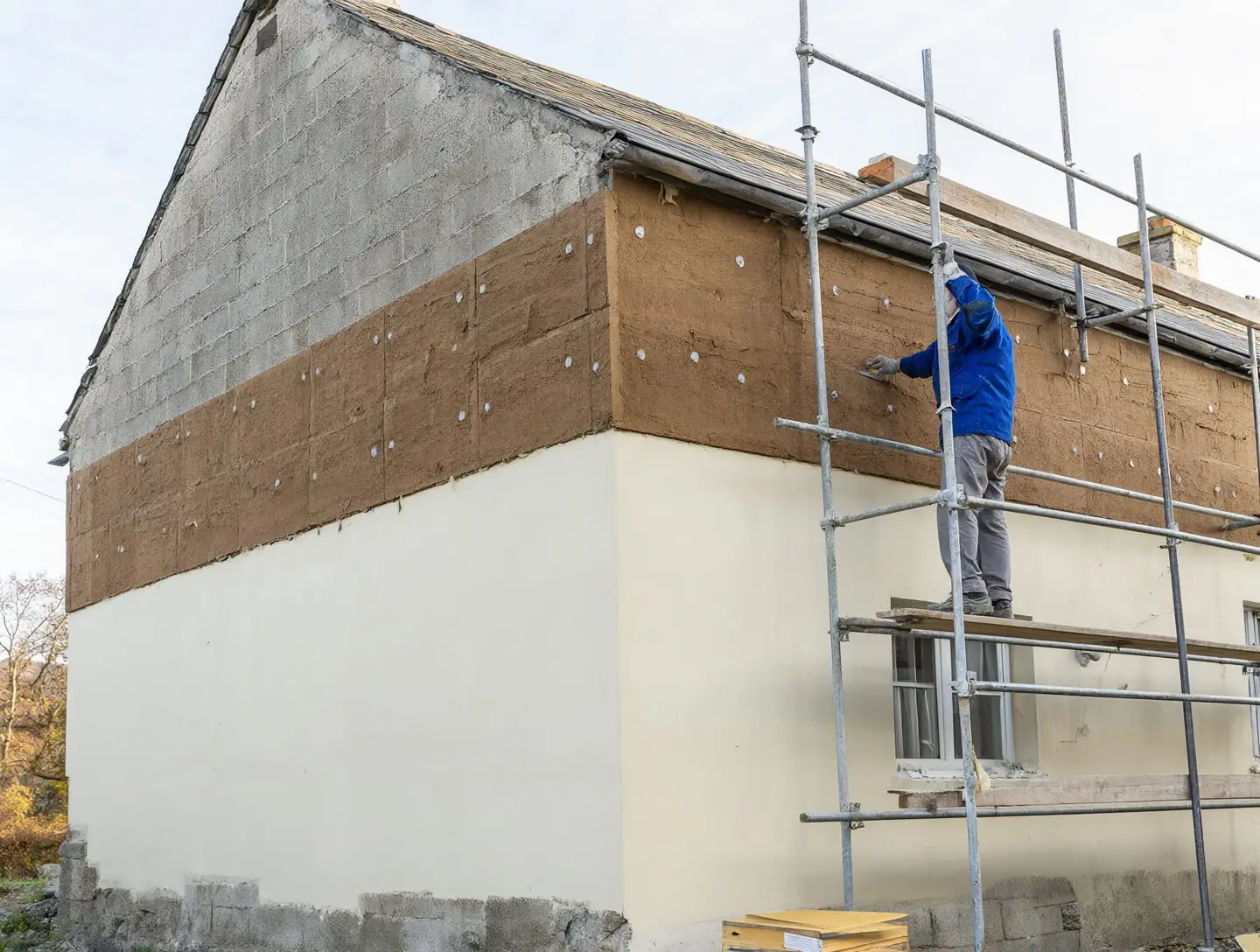 Une façade sous échafaudage, couverte de panneaux de fibre de bois, dont le bas est déjà enduit à la chaux.