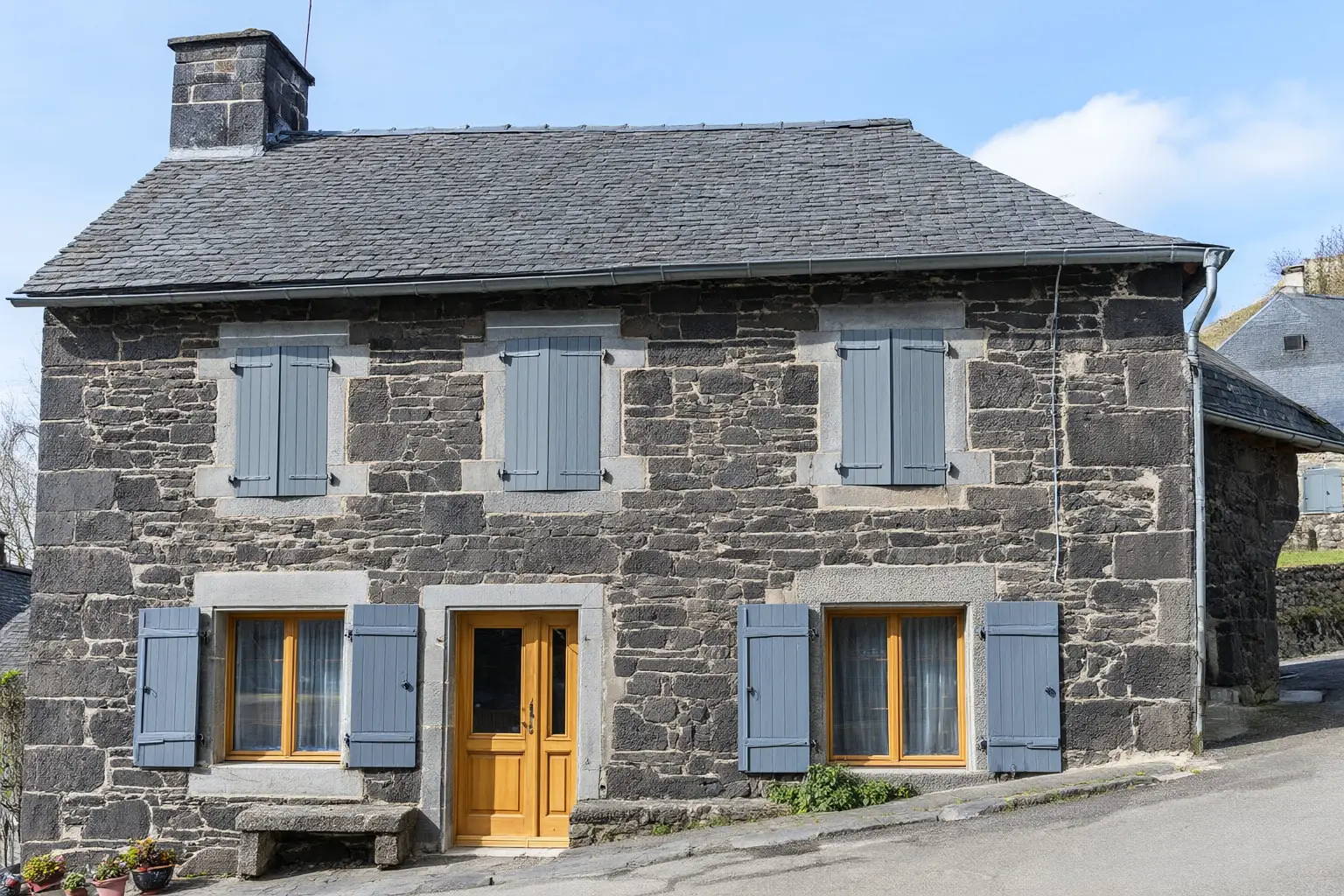 La même maison après travaux : pierre volcanique apparente, joints clairs à la chaux, fenêtres et volets neufs.
