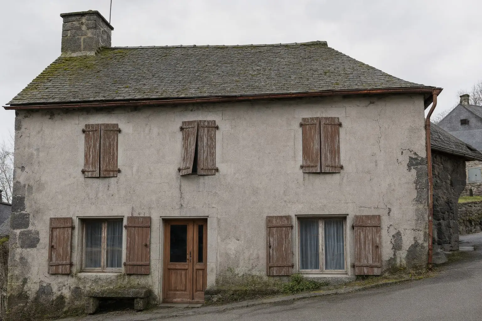La maison avant travaux : façade couverte d’un vieil enduit ciment gris, taché et fissuré.