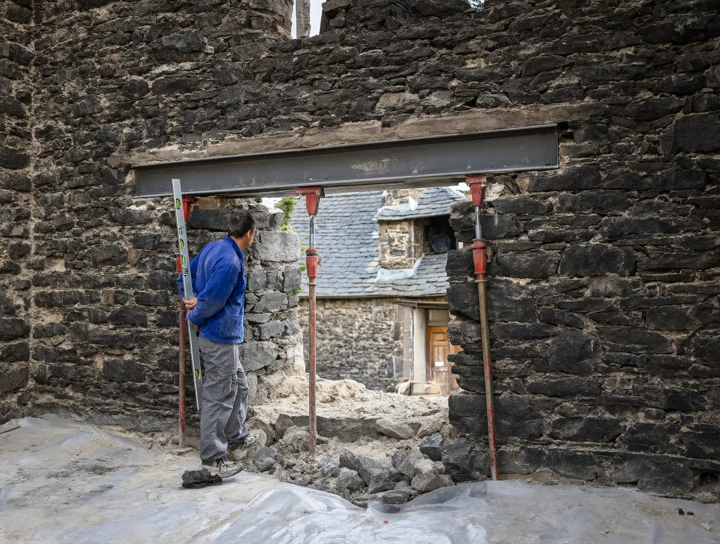 Une ouverture neuve dans un mur porteur en pierre, soutenue par un linteau en acier et des étais rouges.